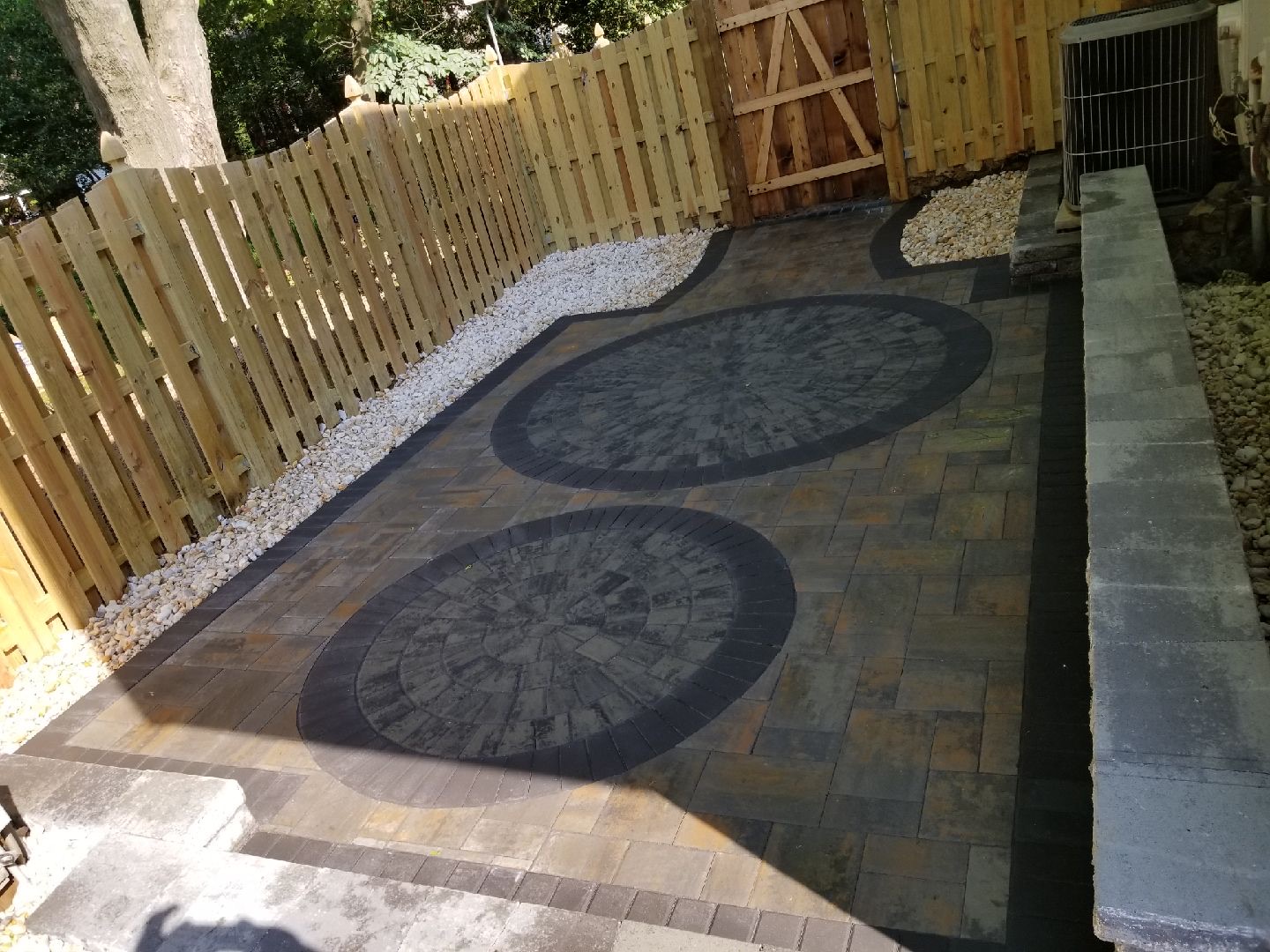 A patio with a wooden fence and two circular stepping stones